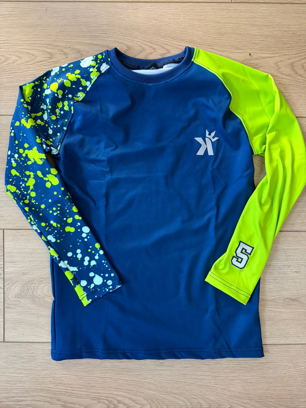 Navy blue long sleeve shirt with a neon green sleeve and a blue-and-white paint splatter print sleeve featuring the number 5, laid flat on a wood floor.