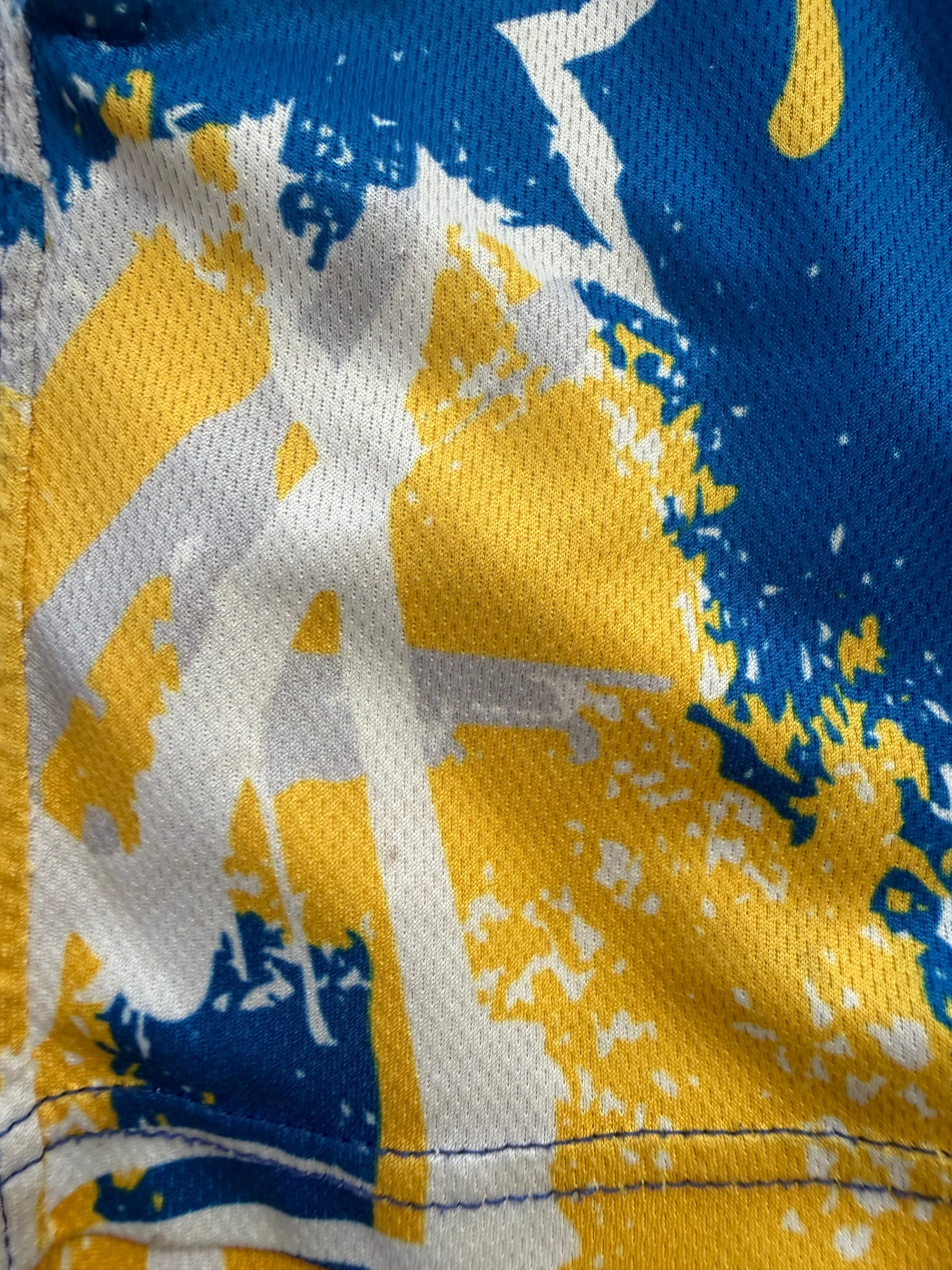 Close-up of blue, yellow, and white abstract paint splatter print fabric texture on custom mesh athletic shorts.