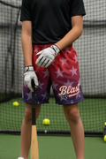 Young athlete wearing red-to-purple ombre star print baseball shorts, holding a bat in an indoor batting cage.